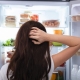 Donna con capelli lunghi che si gratta la testa e guarda in frigo